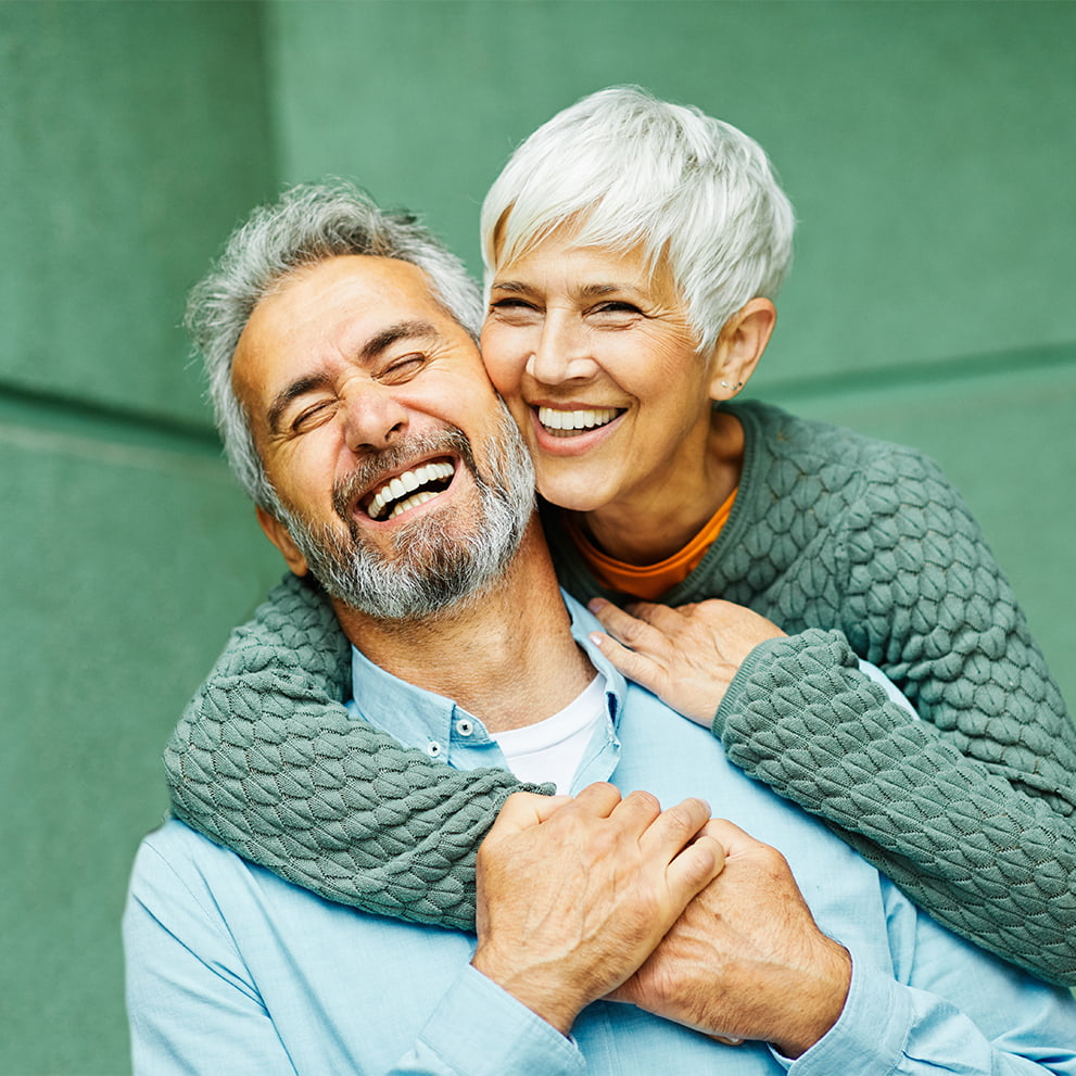 Happy older couple embracing and smiling with visible healthy teeth, suggesting themes of dental wellness, senior oral care, and confidence in mature smiles.