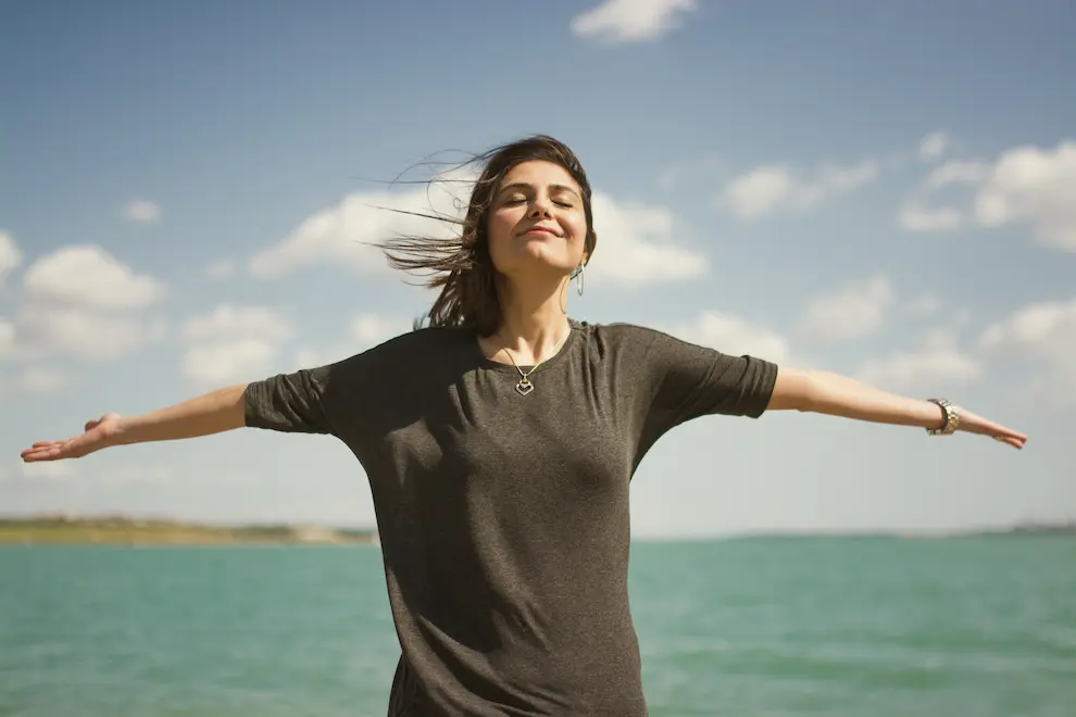 Woman smiling near the ocean while enjoying the sun with her eyes closed
