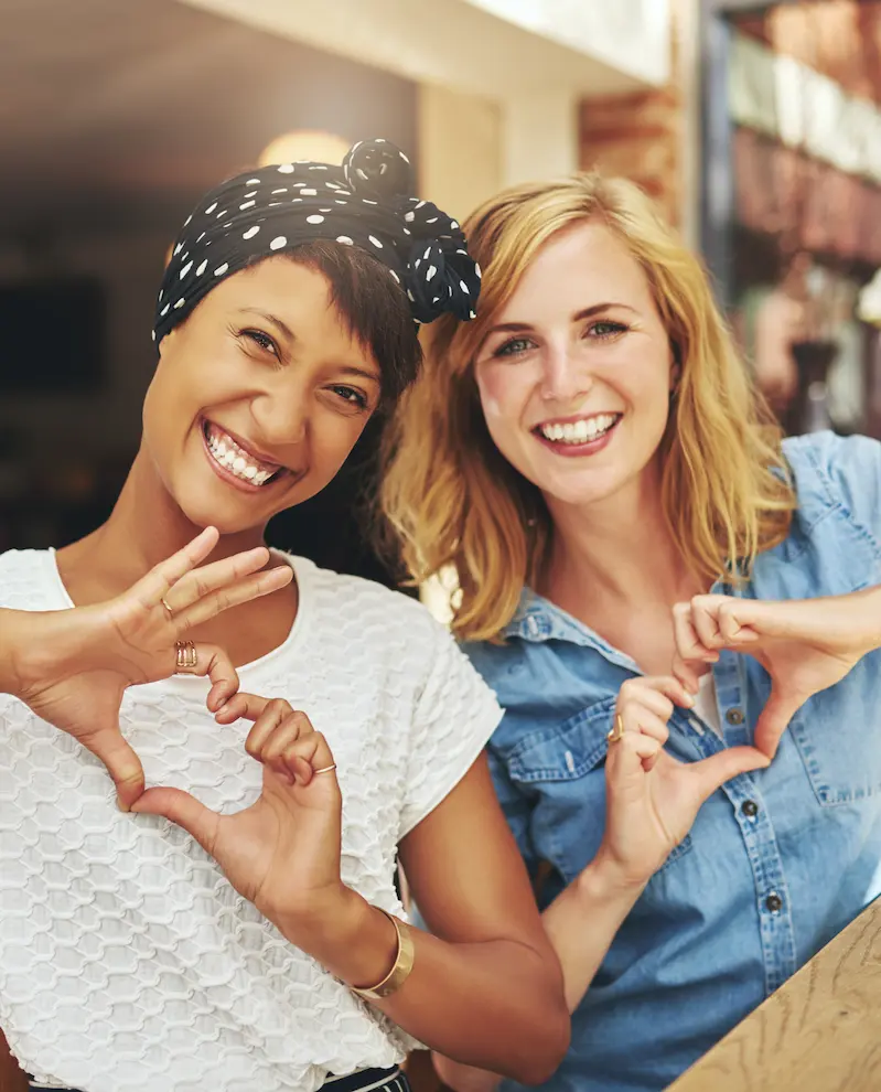 Two women smiling and making heart shapes with their hands