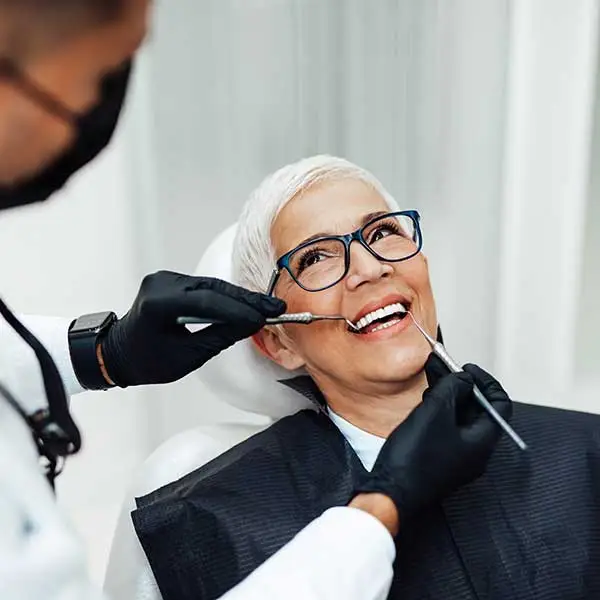 Older smiling woman sitting in a patient chair while a dentist works on her teeth